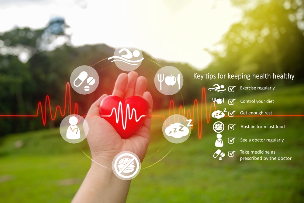 An infographic showing a hand holding a red heart model surrounded by health-related icons and a checklist of tips for maintaining heart health, set against a blurred green park background.
