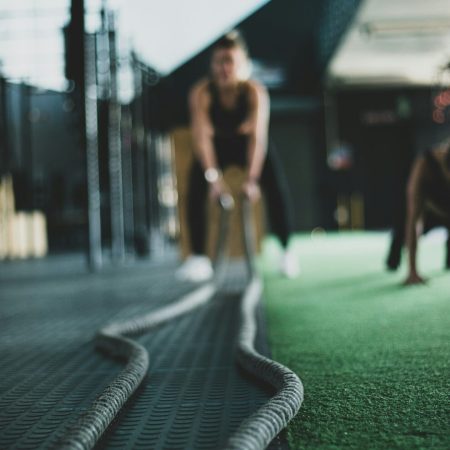 A low-angle, selective focus shot of battle ropes snake across a gym floor, with two blurred women working out in the background.
