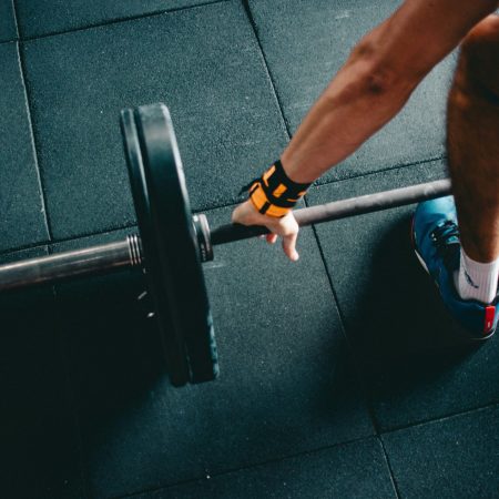 An overhead, cropped shot of an athlete gripping a loaded barbell on a rubber gym floor.