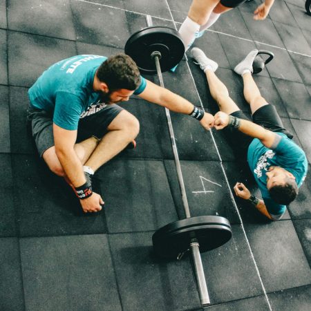 An overhead view of two male athletes sharing a fist bump over a barbell while resting on a rubber gym floor.